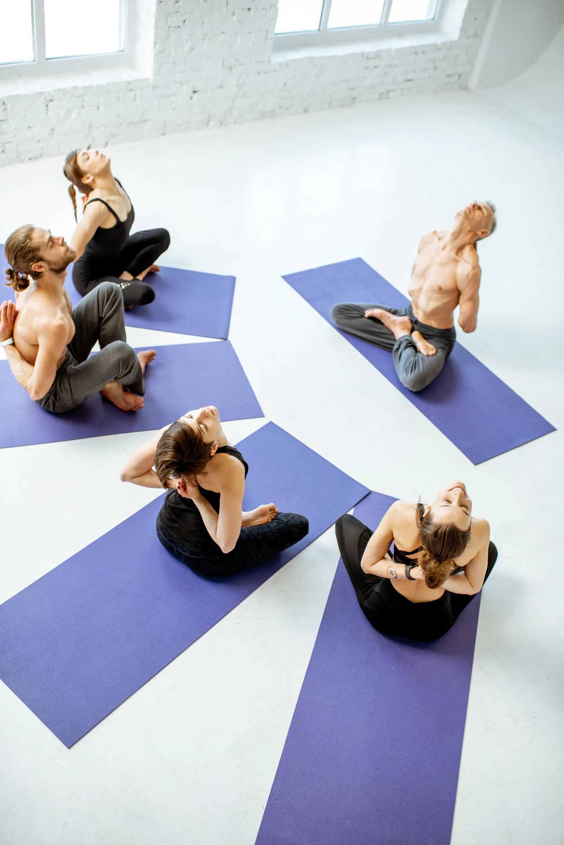 Foto vertical de estudio de pilates o yoga — instructor guiando a grupo de 3-4 personas en colchonetas, luz natural.